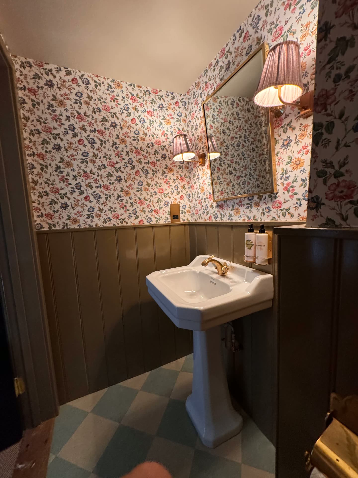 A floral wallpapered cloakroom with brass fittings at The Norman Knight